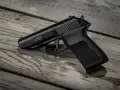 Czarny pistolet gazowy P.M.G.-23 leżący na drewnianym blacie.