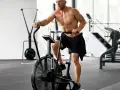 Mężczyzna ćwiczy na rowerze stacjonarnym typu air bike w siłowni.