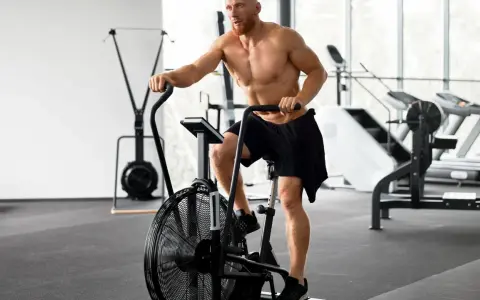 Mężczyzna ćwiczy na rowerze stacjonarnym typu air bike w siłowni.