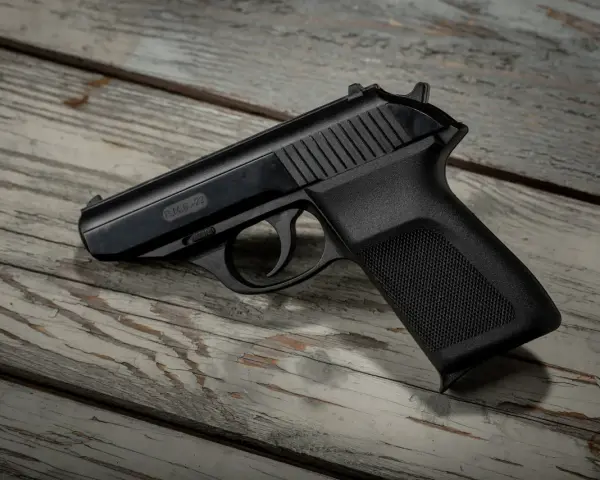 Czarny pistolet gazowy P.M.G.-23 leżący na drewnianym blacie.